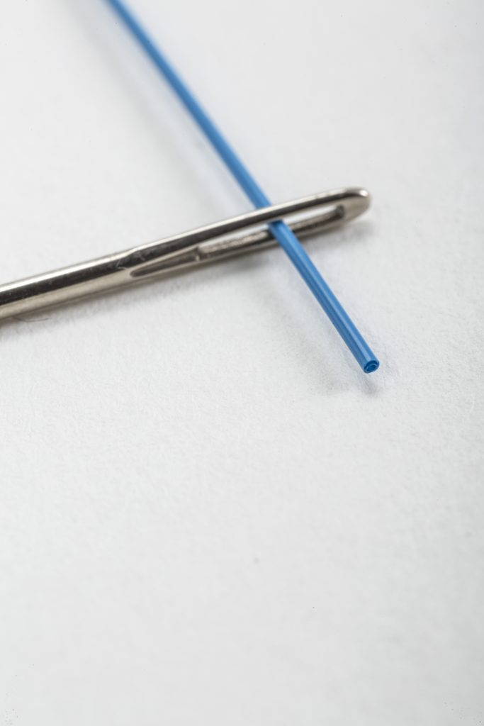 multi-lumen tube with cyclops design threaded through eye of a needle for size comparison