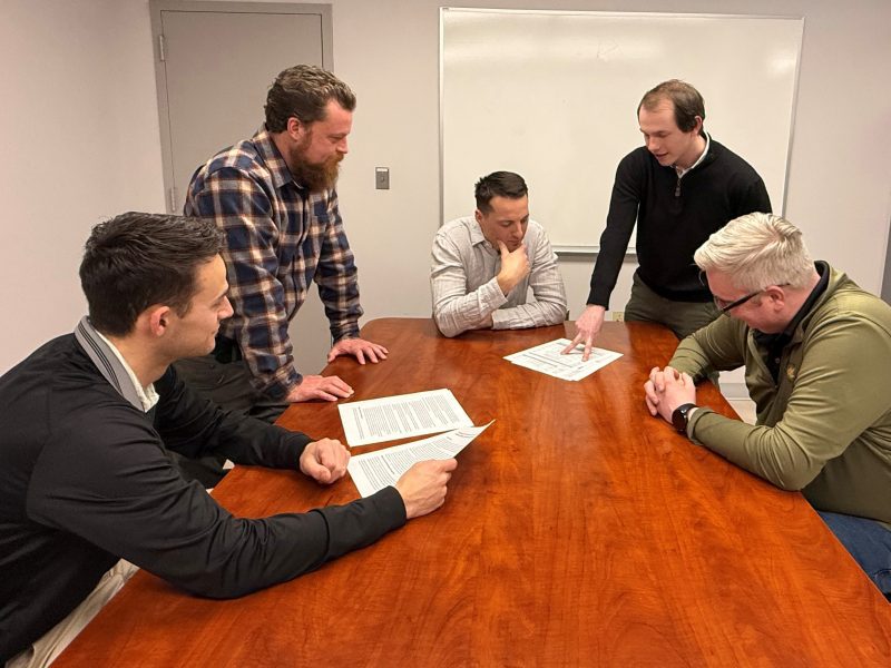 five male engineers around a table looking at documents